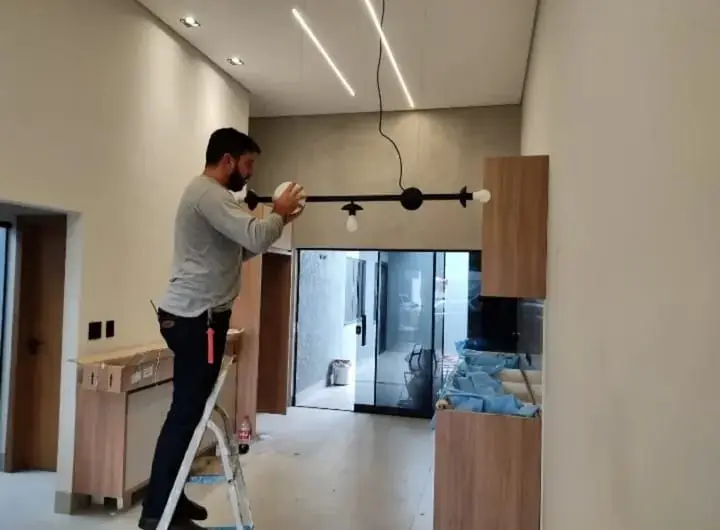 Eletricista ajustando luminária em ambiente interno com linhas de LED no teto.