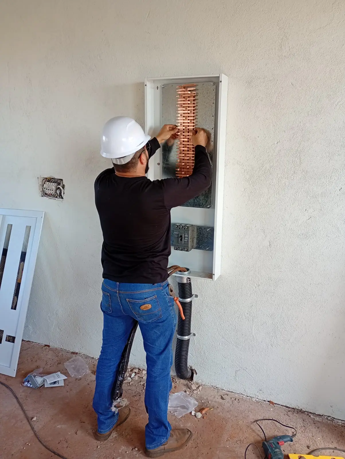 Eletricista trabalhando em instalação elétrica embutida na parede.