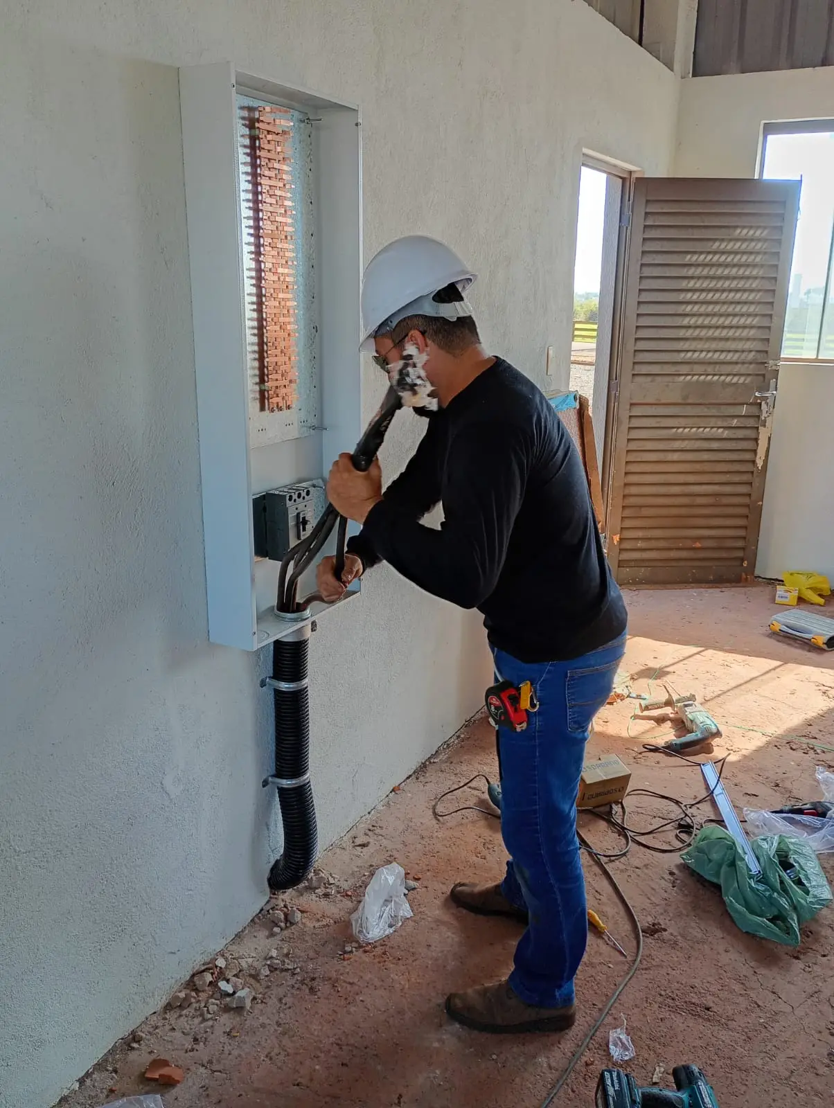 Eletricista organizando cabos em instalação na parede.