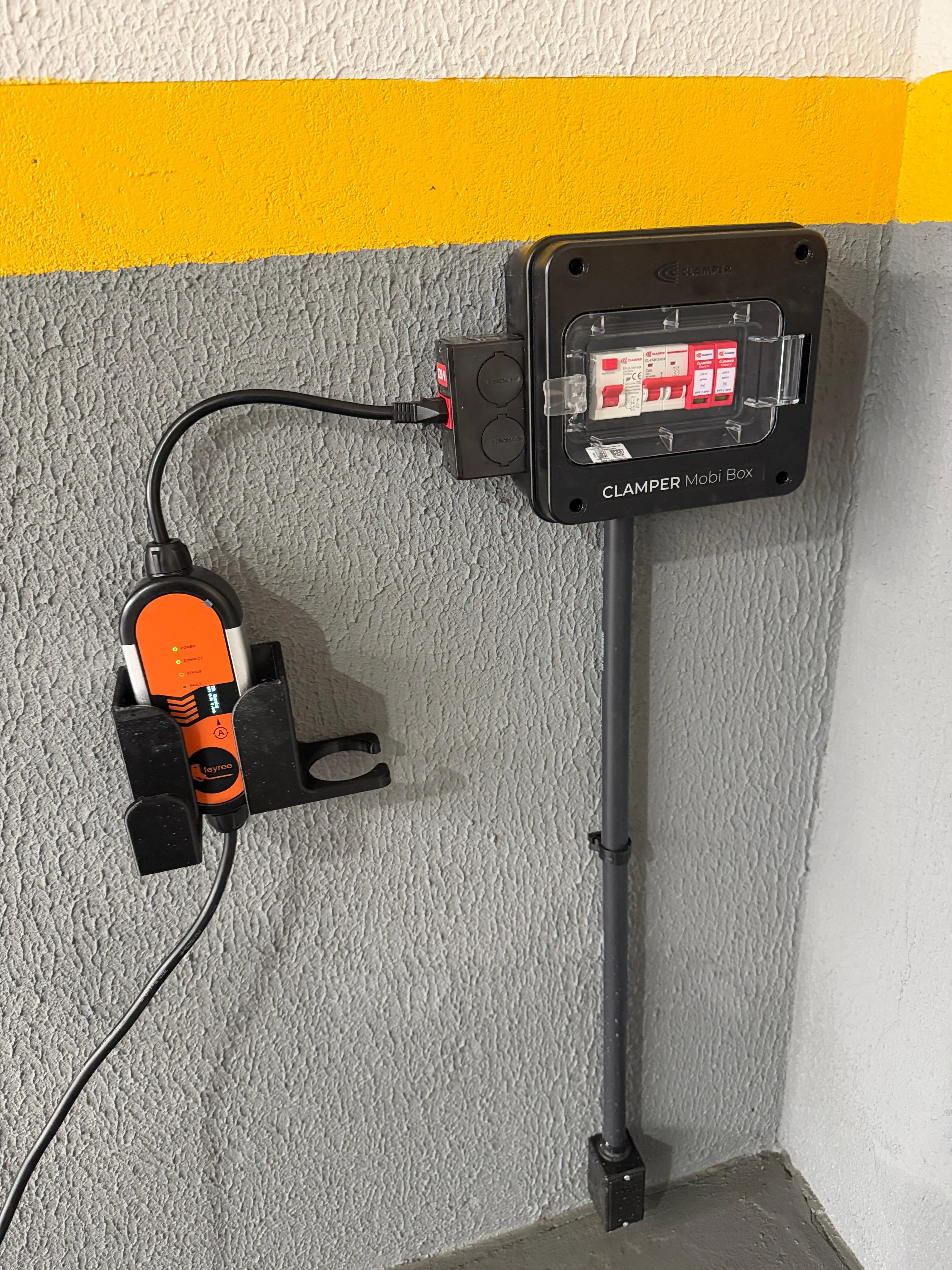 Caixa de proteção com disjuntores e carregador portátil instalados na parede.