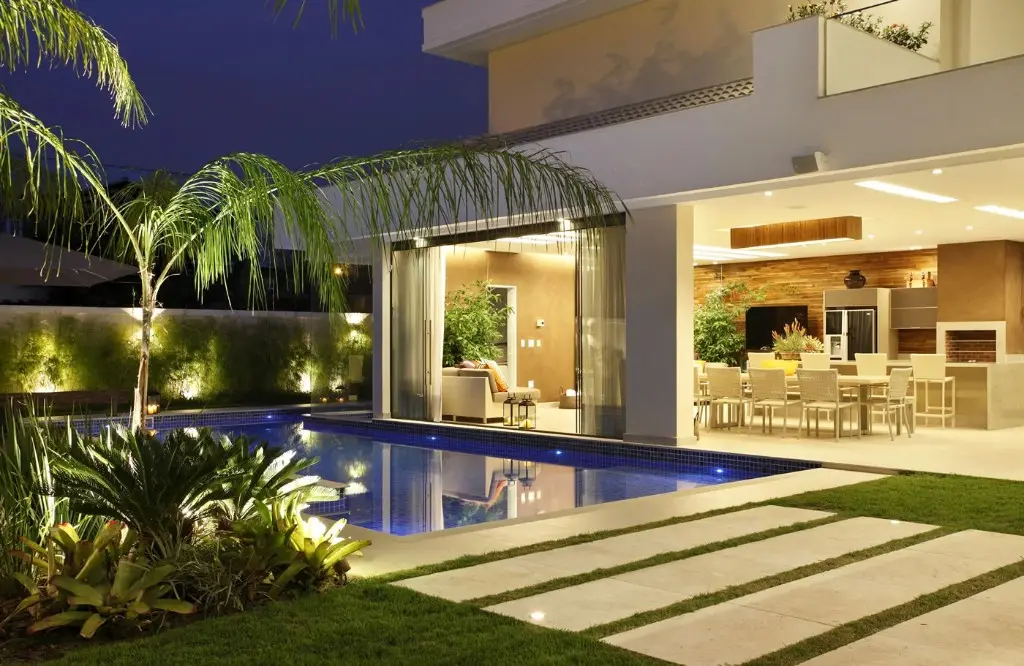 Casa com iluminação interna e externa à noite, piscina e área de estar.