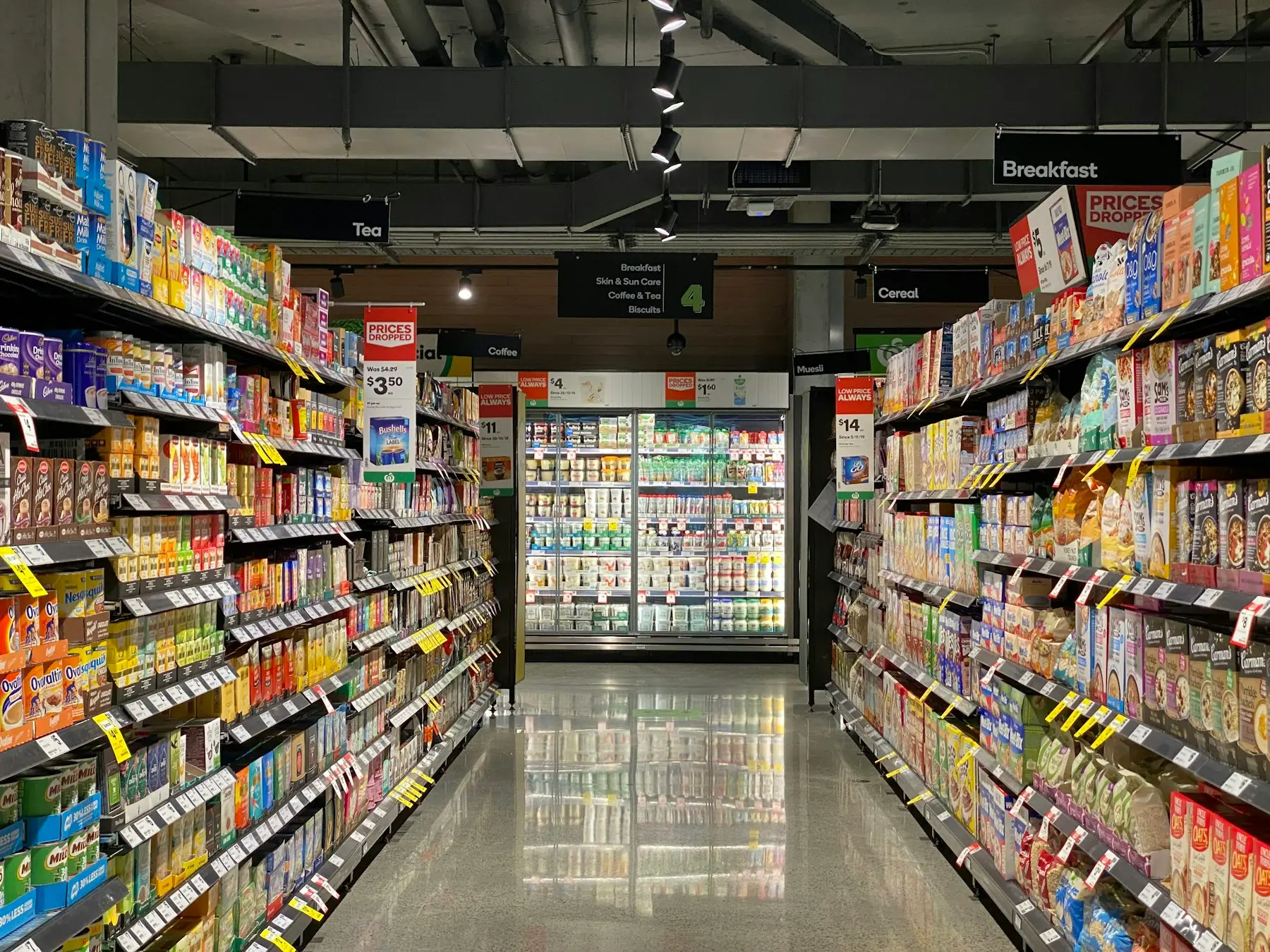 Corredor de supermercado com iluminação e câmara fria ao fundo.