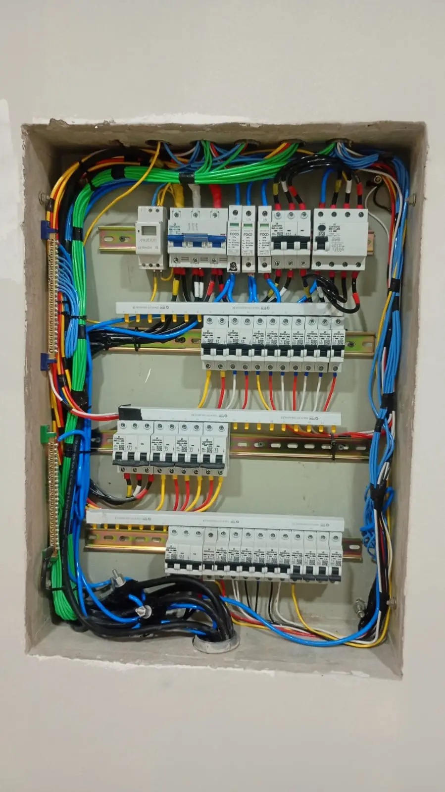 Quadro elétrico embutido com fiação e disjuntores organizados.