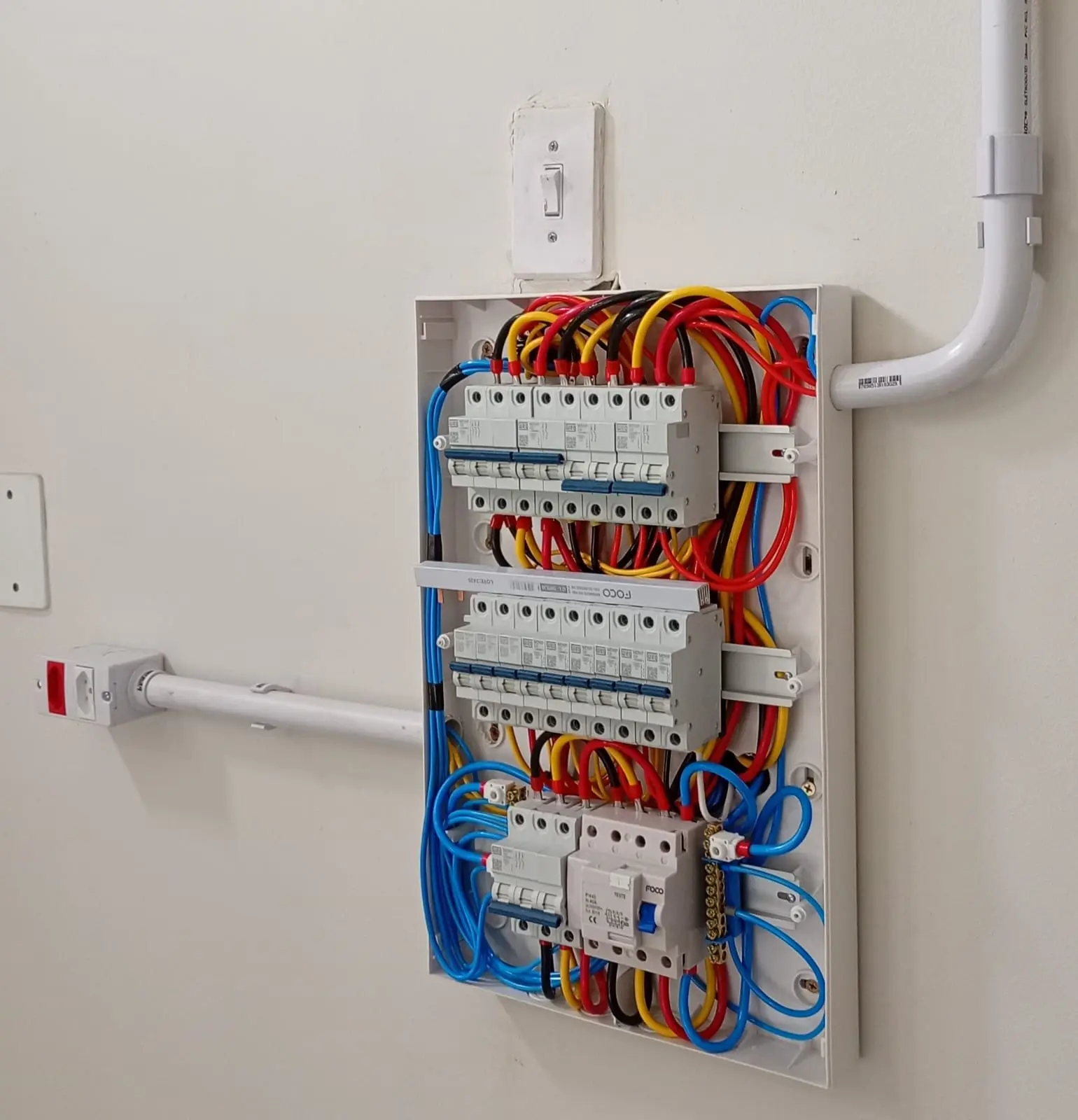 Quadro elétrico embutido com circuitos e conduítes organizados.