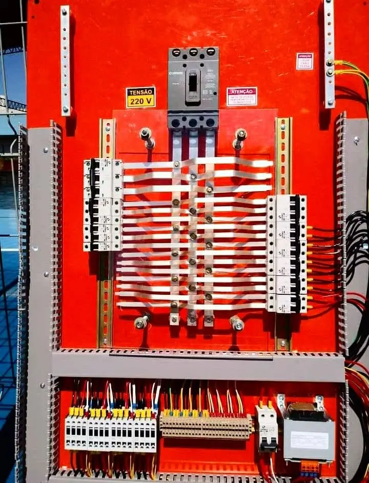 Painel elétrico vermelho com disjuntores, cabos e barramentos.